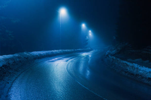 A wet winding road in a foggy and snowy mountain at night.