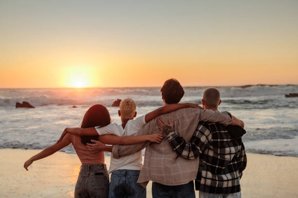 istock Friends hugging and watching golden sunset at beach 2196735648