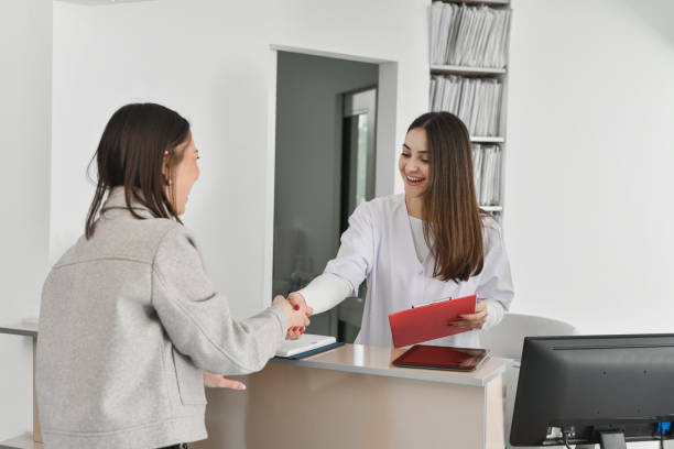 istock Friendly Female Medical Receptionist Greeting Patient and Assisting With Check-In Process and Forms 2196740628