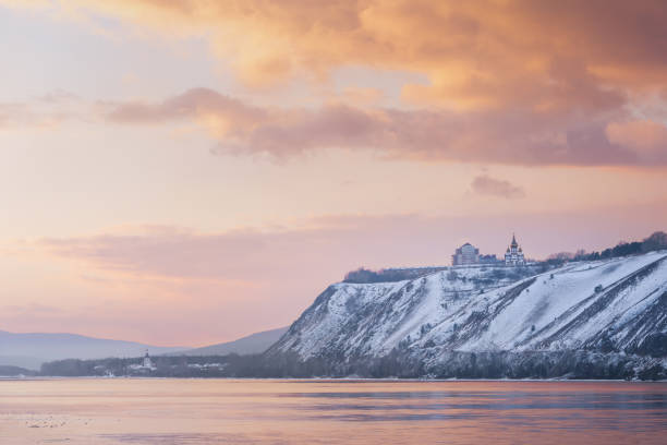 Winter landscape - a Russian Orthodox church snow-covered high bank of the Yenisei River in Krasnoyarsk, Russia. Beautiful view of the Yenisei river at orange sunset stock photo