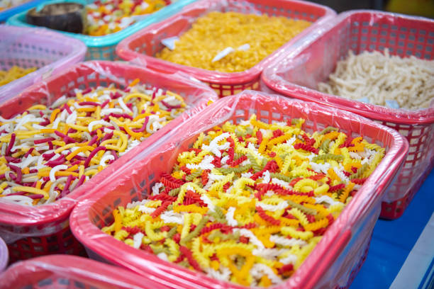 Colorful macaroni, pasta, helical corkscrew fusilli, vegetable flat noodles in large plastic basket with clear liner and desiccant bag at local market in Can Tho, Vietnam, organic raw ingredient. Asia
