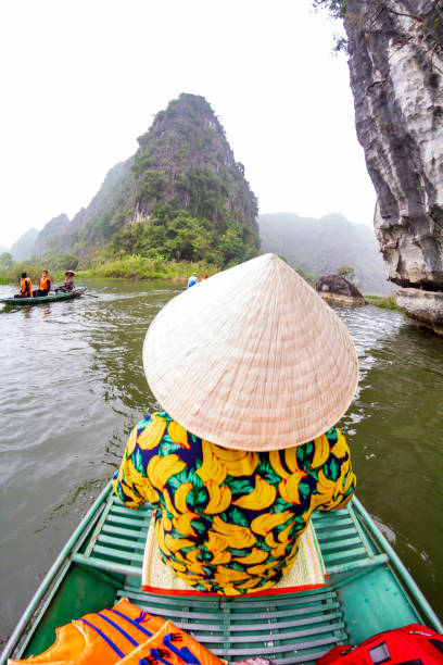 istock Tourist wearing a traditional vietnamese conical hat navigating Tam Coc river in Ninh Binh, Vietnam 2196741864