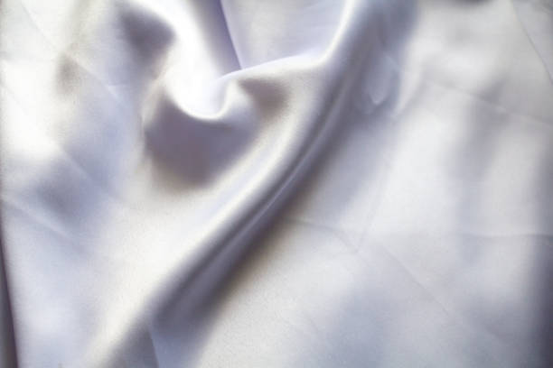 A soft white cloth with gentle folds and a smooth texture placed against a clean background. The fabric exudes purity and elegance, making it ideal for textile, fashion, and home decor concepts.