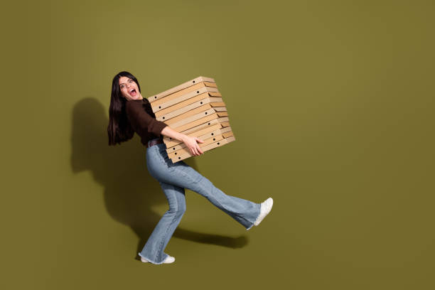 istock Young stylish woman balancing pizza boxes on a khaki background 2196746495