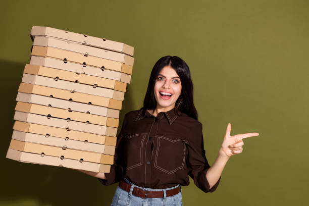istock Joyful woman holding large stack of pizza boxes pointing excitedly with finger against khaki green background 2196746521