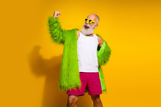 istock Confident senior man in eccentric green fur coat posing on yellow background, celebrating individuality and vibrant style. 2196748508