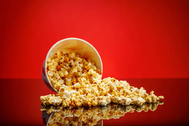 A box of fluffy popcorn against a vibrant red background, showcasing a classic striped design. The bright colors create an inviting, playful atmosphere perfect for a snack