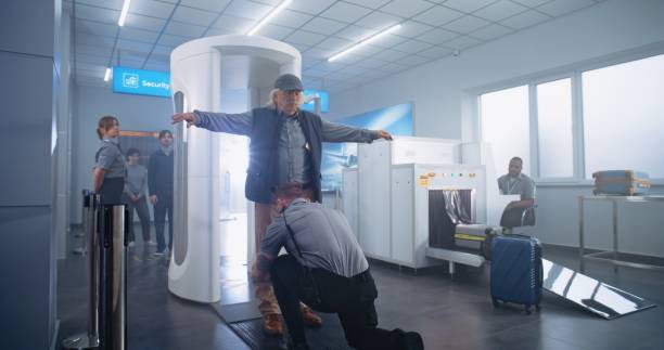 Airport Terminal: Elderly Man Walks Through Metal Detector Gates, Takes Luggage from Conveyor Belt. Security Officer Checks Passenger and Documents for Plane Flight. Diverse Tourists Going on Trips.