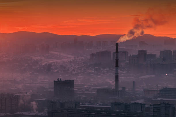 A smoky industrial landscape is illuminated by a vibrant sunrise, highlighting ongoing pollution issues