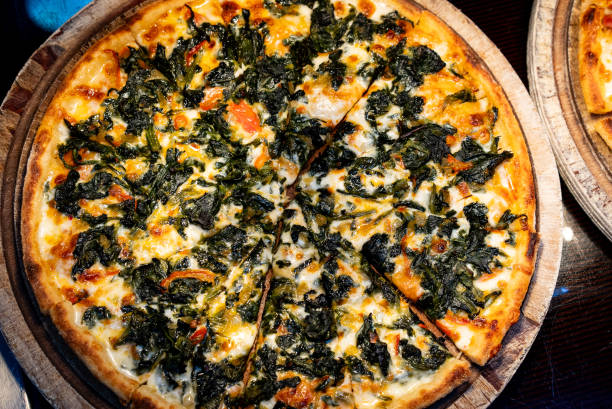 Stock photo showing close-up, elevated view of a large, brown cardboard pizza box displaying a sliced spinach and cream cheese pizza just baked in hot oven, topped with a rich tomato marinara sauce, stringy melted buffalo mozzarella, and spinach and cream cheese  slices.