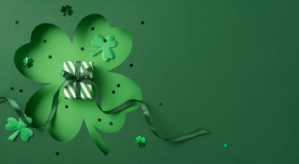 istock Festive St. Patrick's Day image featuring a shamrock cutout adorned with a gift box, ribbons, and small clover-shaped accessories on a green themed background 2196774618