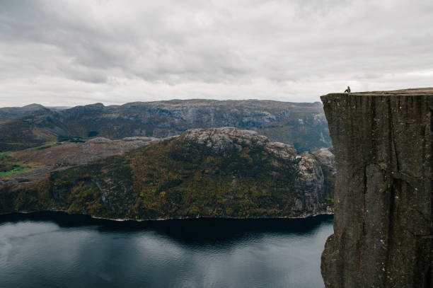 istock Person Sitting on Cliff Edge Overlooking Fjord 2196775906
