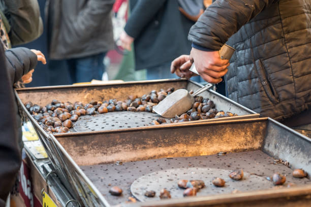 Hands skillfully prepare roasted chestnuts in a vibrant market filled with lively conversations and the allure of fall flavors on a crisp evening.