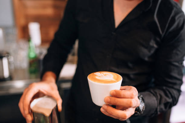 A barista carefully creates latte art with steaming milk, demonstrating professional expertise and artistic skill in a cozy coffee shop environment