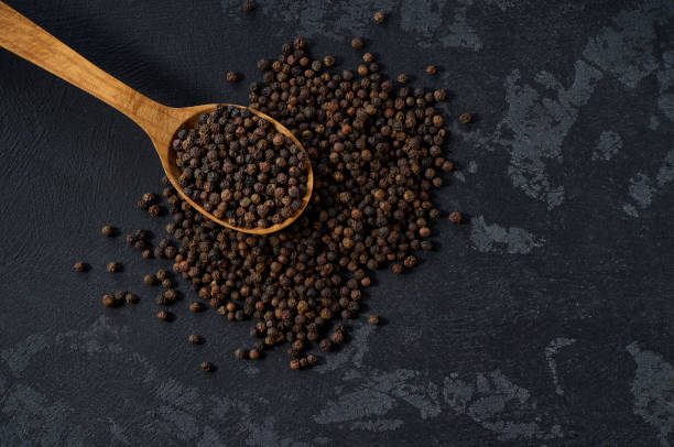 istock black pepper seeds in a wooden spoon on a black stone table, top view. 2196780175