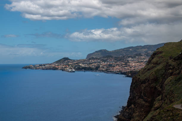View on the calm water of Atlantic ocean from a mountain on the coast. Houses of capital Funchal. Blue sky with white clouds in the spring. Canico, Madeira, Portugal.
