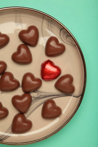 Red chocolate sweets as heart on plate on mint background. Valentine's day concept. Vertical