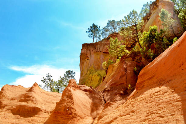 Picturesque rocks from natural ocher. The village of Roussillon. Provence, France. Brightly colored rocks lit by the midday sun. The rocks are covered with forest.