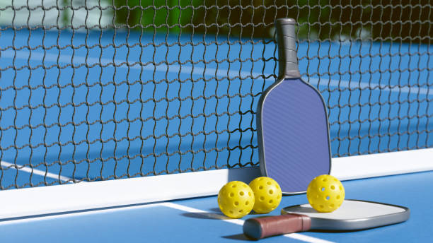 A pickleball paddle and balls resting by the net on a blue court, ready for a game. 3d rendering