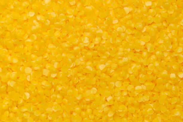 Top view of bright yellow beeswax pellets, ideal for candle making or crafting. Smooth texture, wax background.