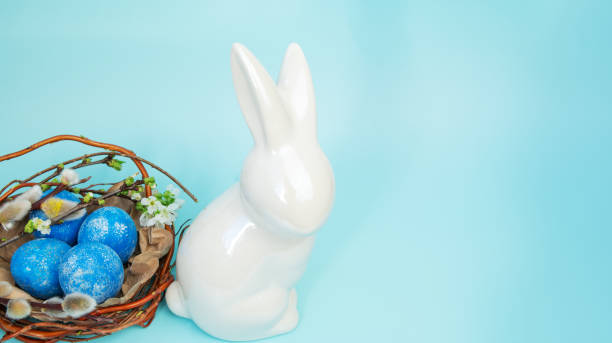 istock Easter background with a figurine of a white rabbit and painted blue eggs in a nest, willow branches. 2196808933