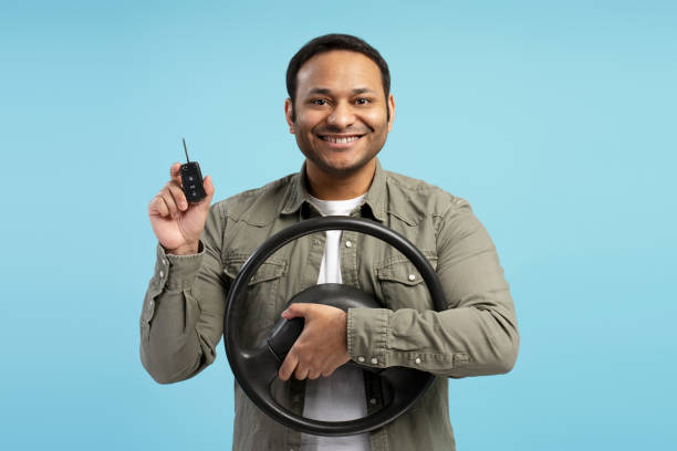 istock Happy driver holding steering wheel and car key on blue background 2196815431