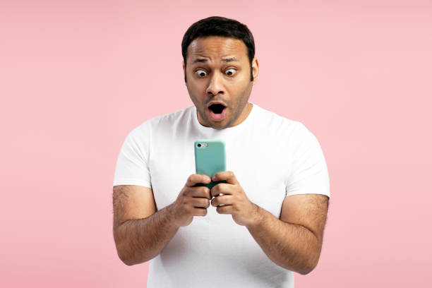 istock Shocked man reading news on smartphone on pink background 2196815478