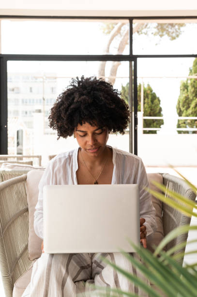 Young woman sitting comfortably in an armchair, concentrating on her laptop, working from home