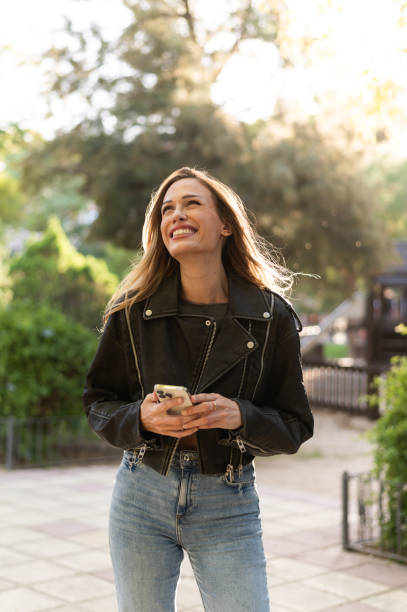istock Smiling woman holding smartphone looking up in a park 2196817134