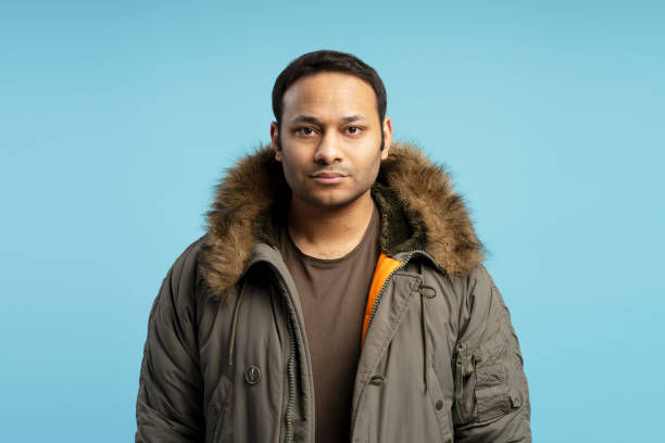 istock Young man wearing winter coat posing on blue background 2196818444
