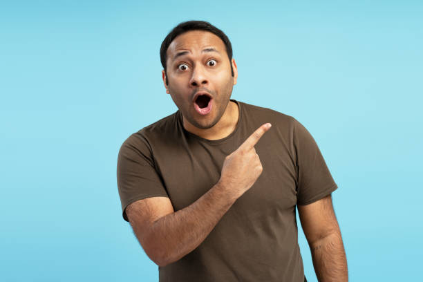 Surprised man pointing finger showing something exciting on blue background