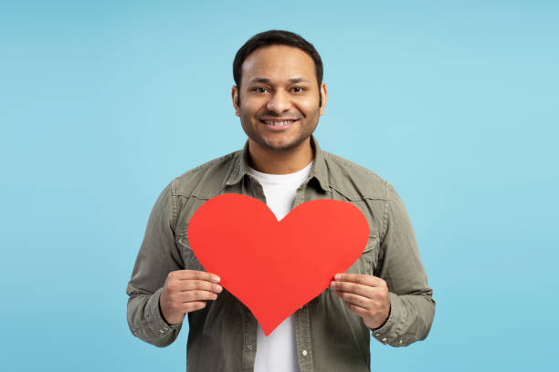 istock Smiling man holding big red heart on blue background 2196818563