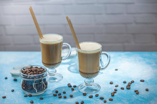 istock Two latte served in elegant glass cups with coffee beans and wooden stirrers on blue table 2196820708