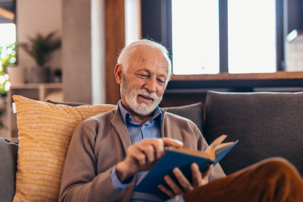 istock Senior man relaxing on sofa reading a book at home 2196821276