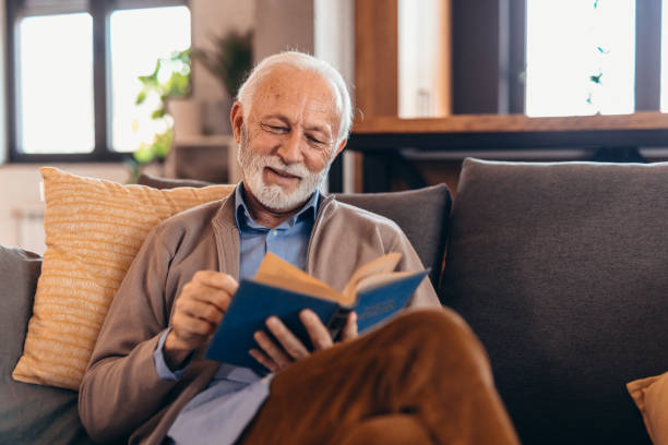 istock Senior man enjoying reading a book on the sofa at home 2196821278