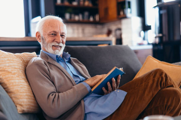 istock Senior man relaxing on sofa reading a book and smiling 2196821290