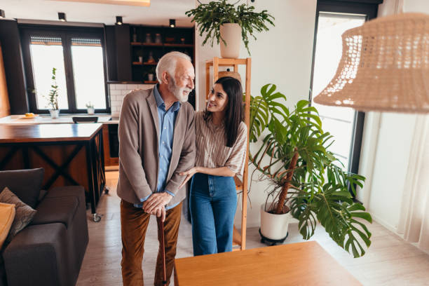 Young woman assisting elderly man with walking stick at home