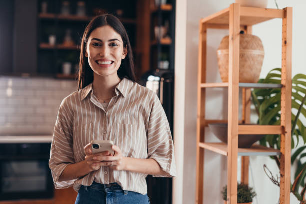 istock Young woman smiling and using mobile phone at home 2196821343