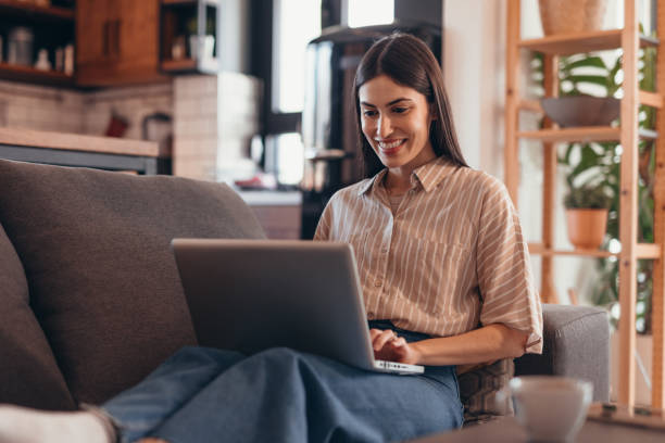 istock Young woman working from home, sitting on the sofa and using a laptop 2196821358