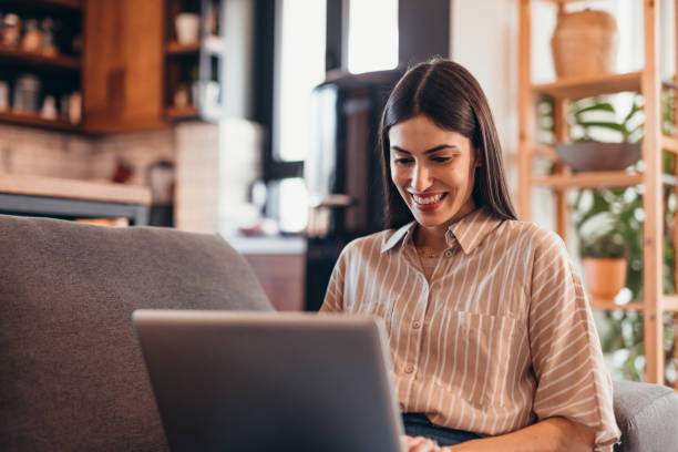 istock Young businesswoman working from home, smiling and using laptop on the sofa 2196821367