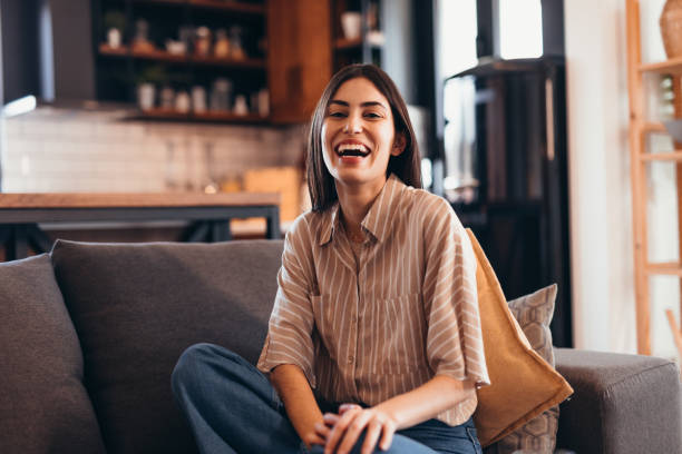 istock Young Woman Laughing While Sitting on Sofa in Living Room 2196821409