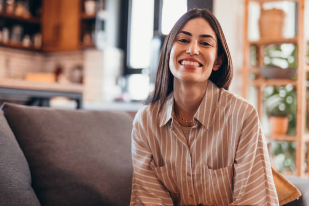 istock Young woman smiling and looking at camera while sitting on sofa at home 2196821416