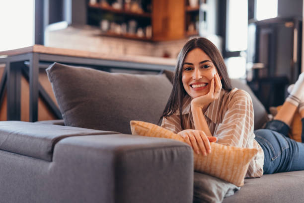 istock Young woman relaxing on sofa, smiling and looking at camera 2196821431
