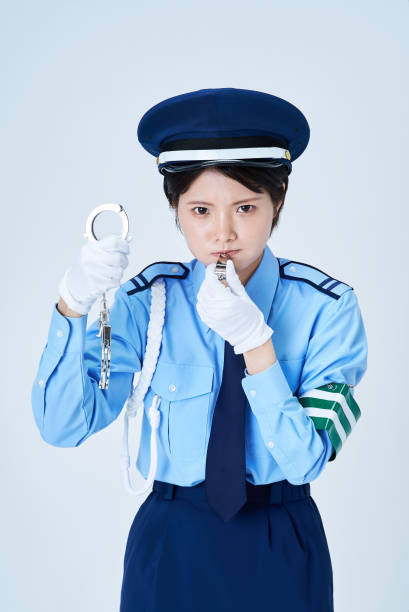 A caucasian female Police Officer with blond hair stands with her arms crossed in front of her police squad car.  Her uniform includes a badge, gun, and a two-way radio.