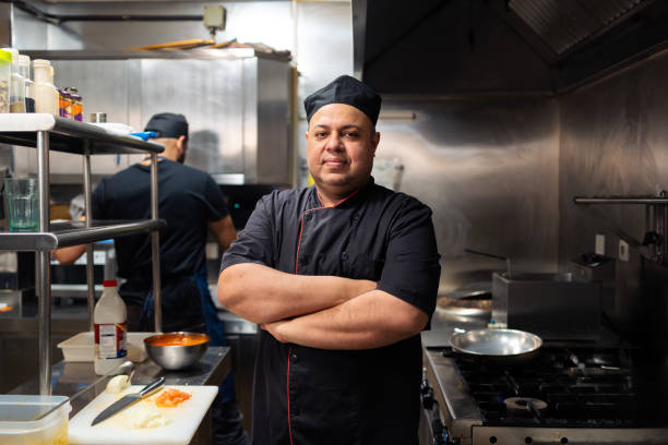 istock Professional Indian chef crossing arms confidently, displaying culinary mastery inside bustling commercial kitchen workspace 2196828305