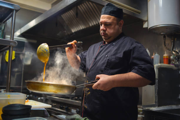 istock Chef pouring steaming sauce into a pan in a bustling commercial kitchen, skillfully preparing a mouthwatering meal filled with flavor 2196828311