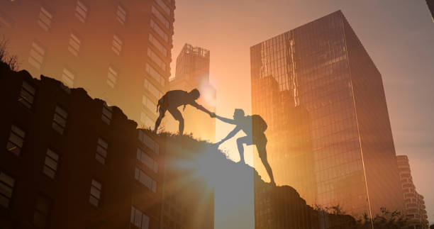 istock Team work, life goals and self improvement concept. Man helping his friend climbing partner up a steep edge of a mountain, 2196829148