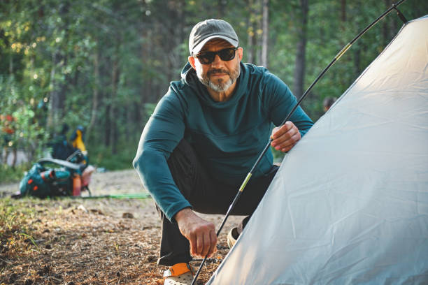 Couple, tent and setting camp with rods in forest for outdoor stay, adventure or travel together. Man, woman and campers with equipment or preparation for safety, shelter or protection in wilderness