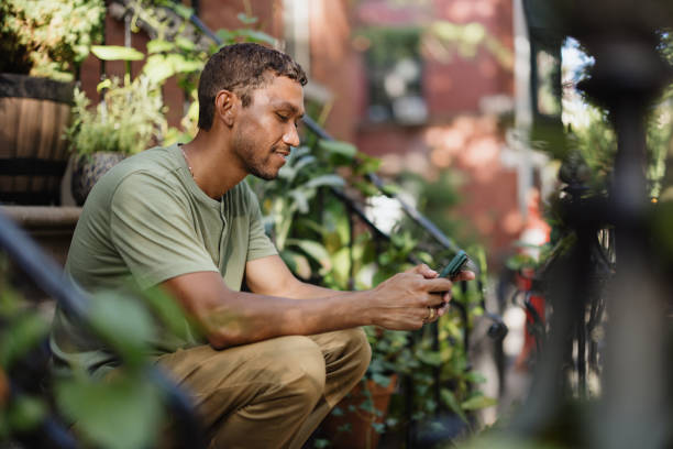 istock Man Sitting Outdoors Using Smartphone in Urban Garden Setting 2196837784