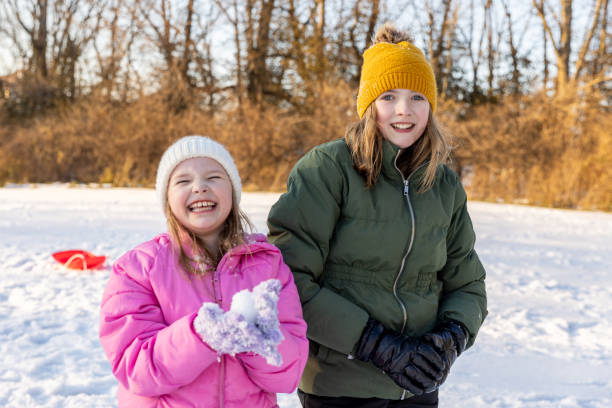 istock Happy elementary age sisters smile while having snowball fight and playing together outdoors on winter day 2196839171